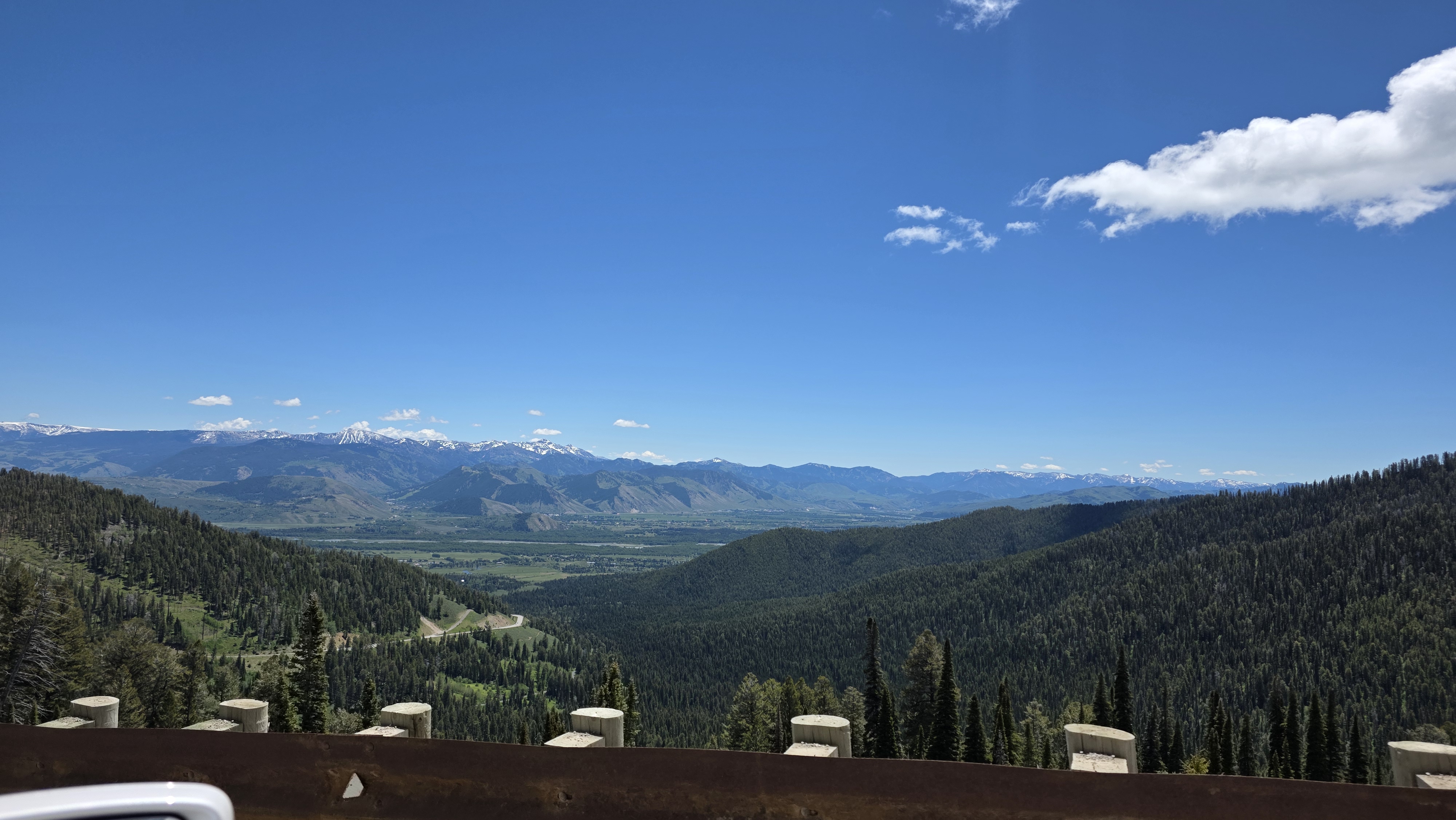 Panoramic view of a mountainous landscape with lush green valleys and snow-capped peaks under a clear blue sky.